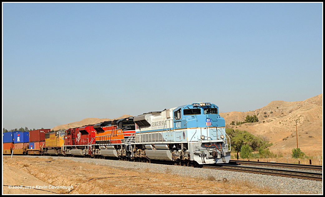 A blue and white locomotive pulls a double-stack train through barren landscape.